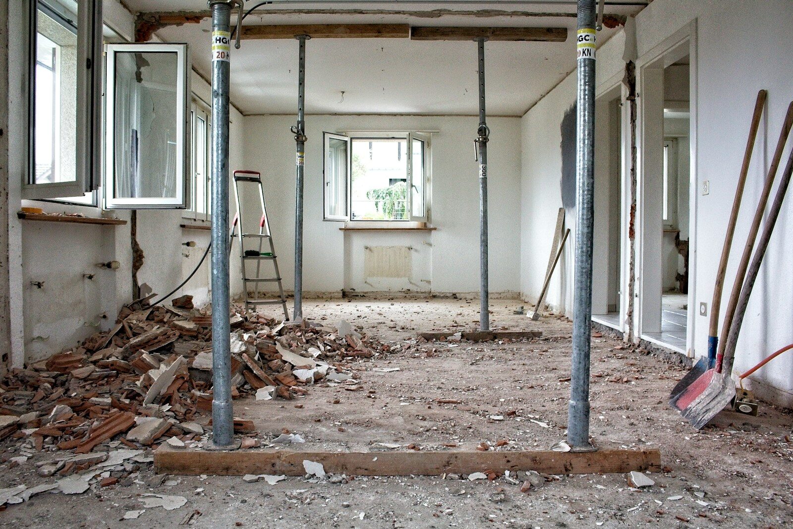 A room under renovation with metal support poles, debris, and tools on the floor